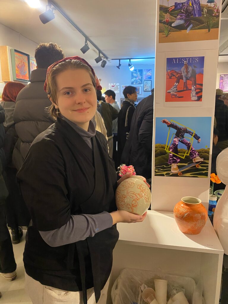 A picture of the artist holding a ceramic object on display in a crowded exhibition space